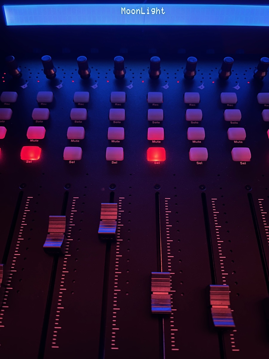 The iCON QCon through the bridge: its display reads MoonLight, its motorized faders stand at the leader's levels, and two pads glow red